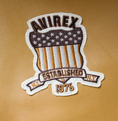 Close-up of Avirex heritage shield chest patch embroidered over the tan leather varsity bomber