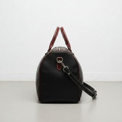 side view black and brown leather weekender bag with detachable strap.