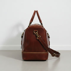 side view brown leather weekender bag showing drop bottom zipper compartment.