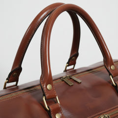 close up of rolled leather handles and brass hardware on brown travel duffle.