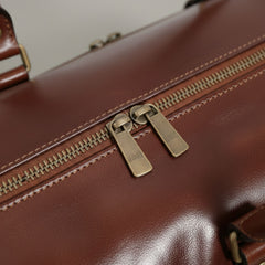 close up of brass metal zippers on brown genuine leather drop bottom bag.