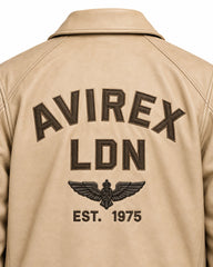 Close-up of cream aviator jacket back showing raised brown lettering, winged aviation emblem and 1975 detail