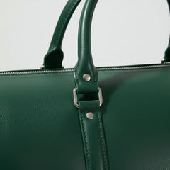 close up of rolled leather handles and metal hardware on green duffle bag.