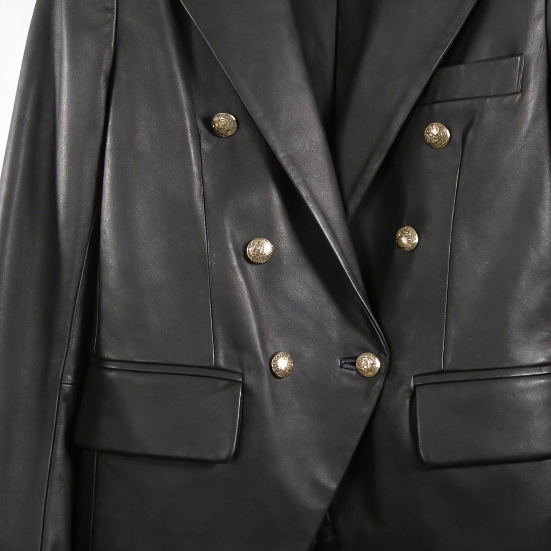 Gold button front and flap pockets on women’s double breasted black leather blazer