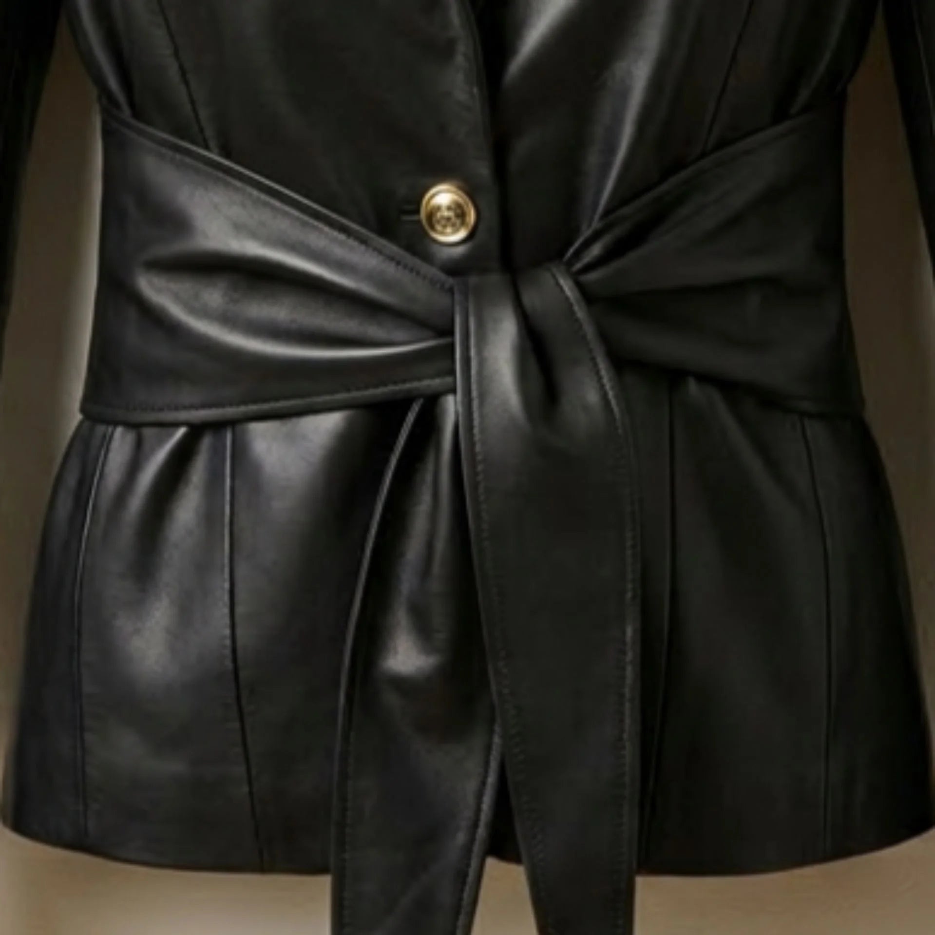 Gold button and tie waist belt detail on women’s black leather blazer