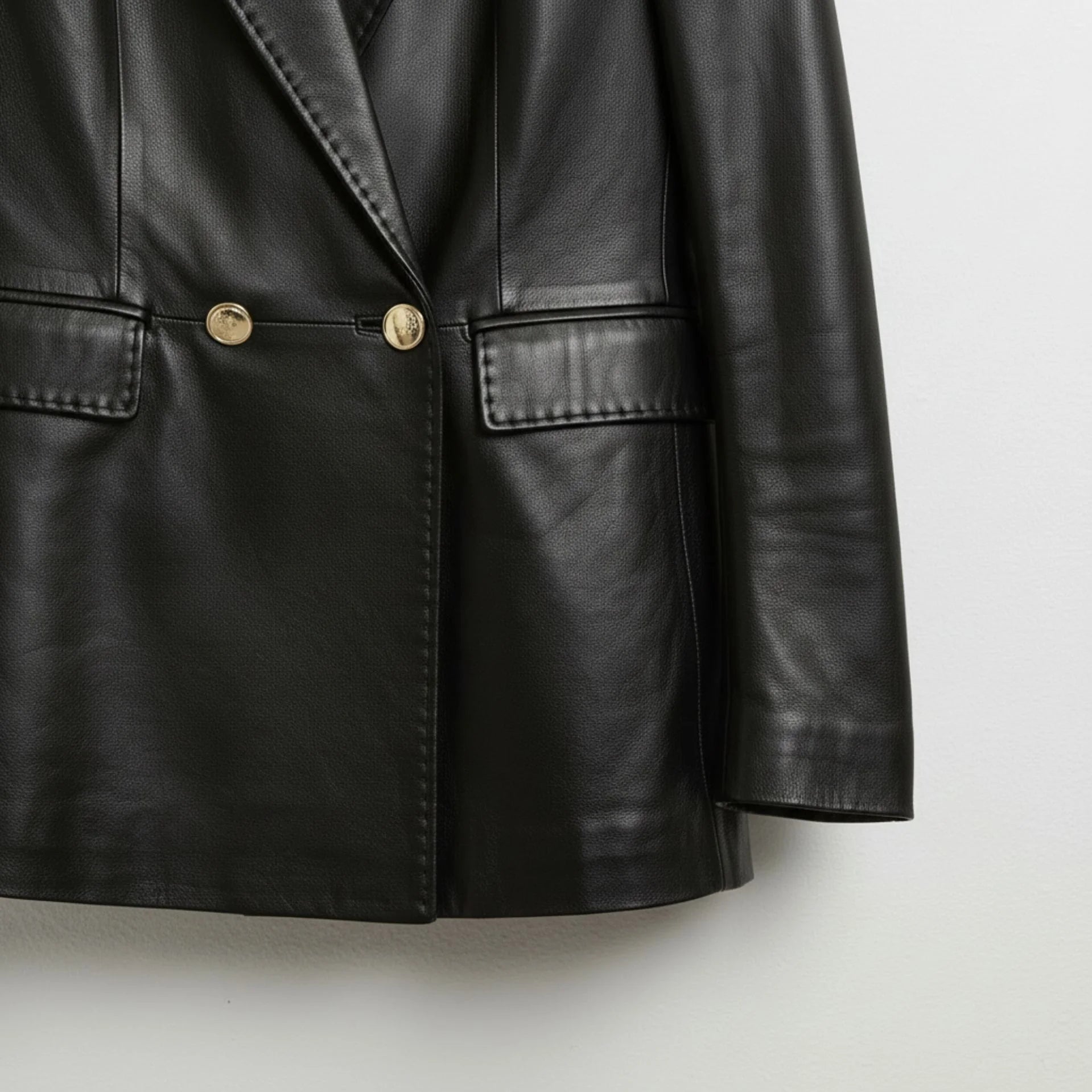 Gold button and flap pocket detail on women’s black leather blazer