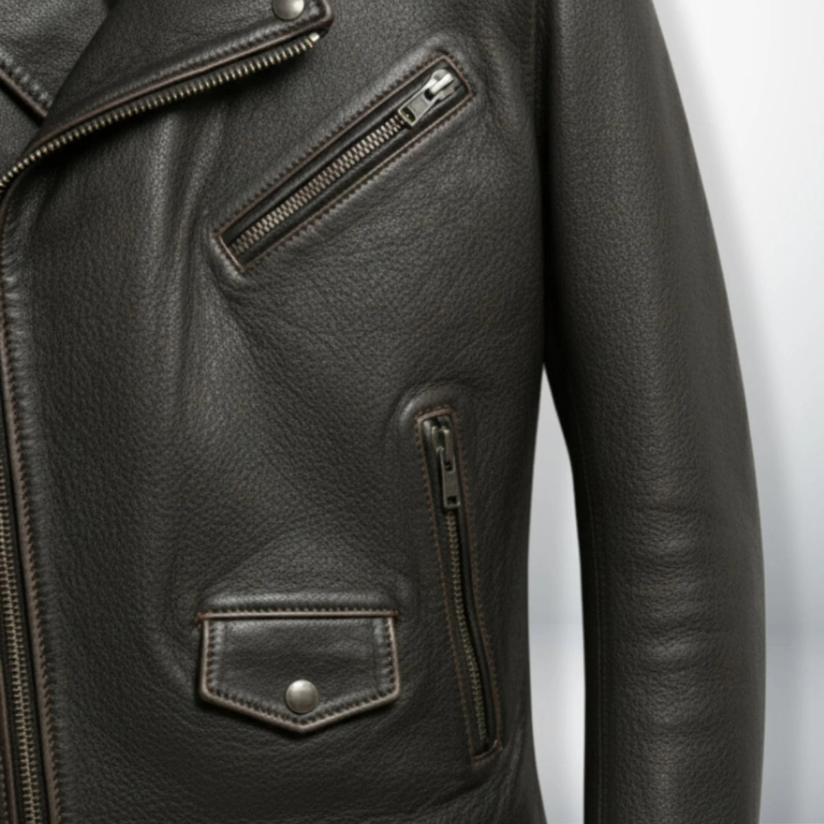 detail of chest zip pocket and flap pocket on men's dark brown leather jacket.