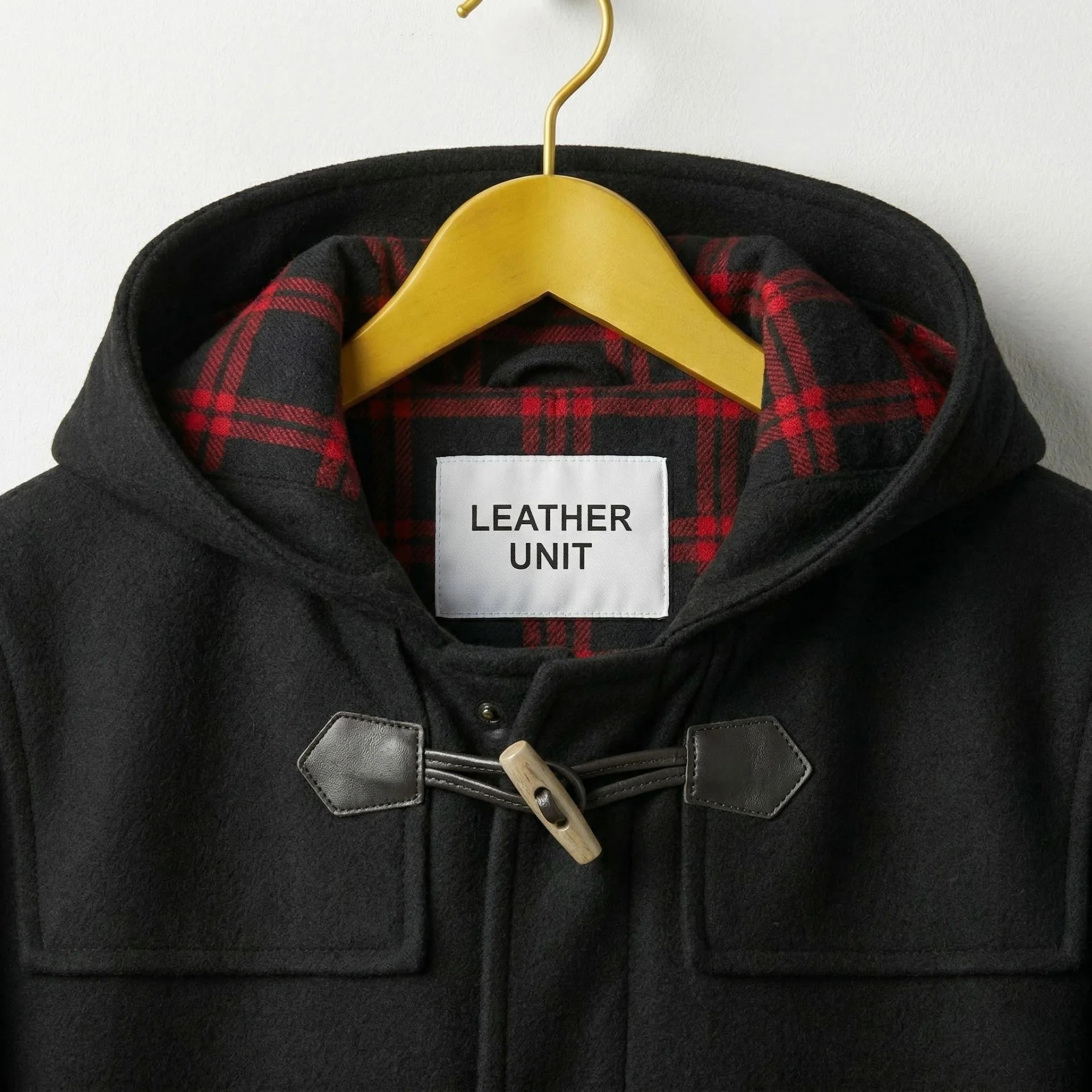Close up of hood with red plaid lining and Leather Unit label on black duffle coat.