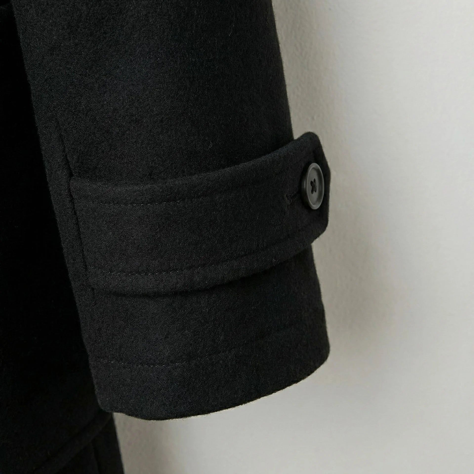 Detail of cuff strap and button on men's black wool duffle coat.