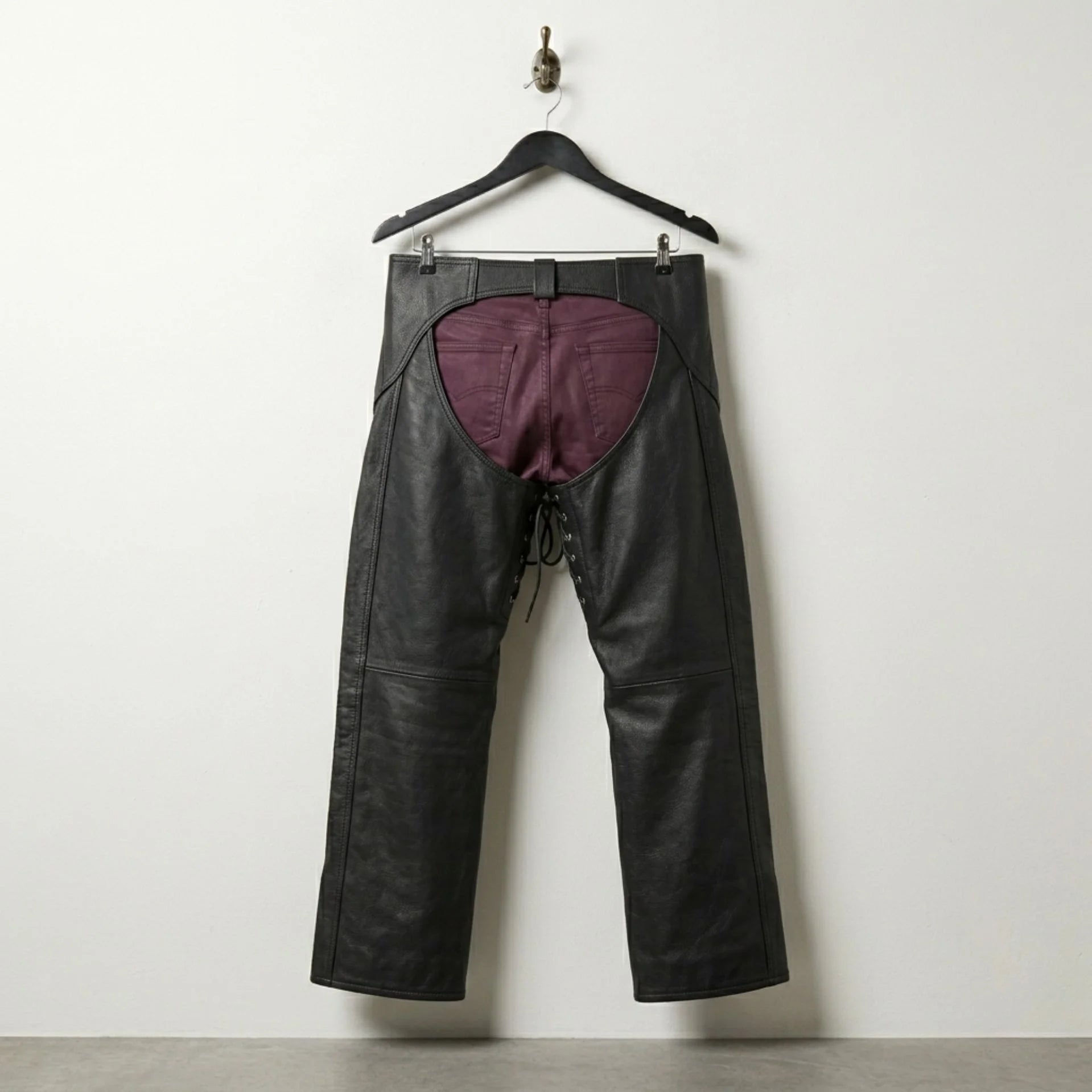 Back view of open back black leather motorcycle chaps worn over burgundy pants