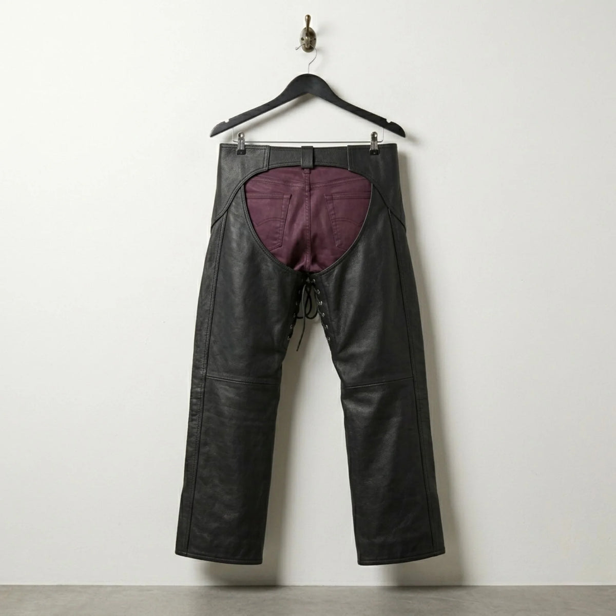 Back view of open back black leather motorcycle chaps worn over burgundy pants
