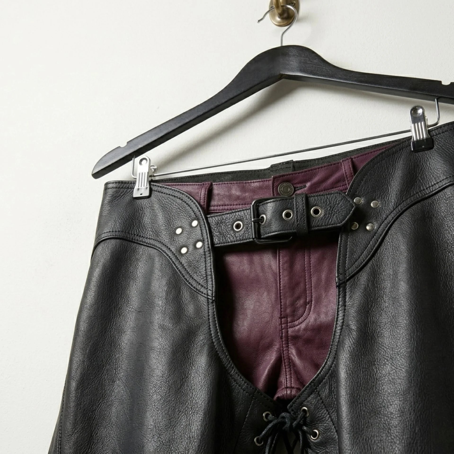 Close-up of waist belt, rivets and burgundy pants under men's black leather chaps