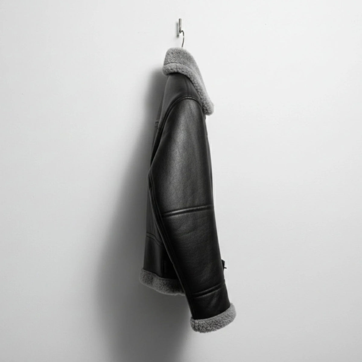 side profile mens black shearling bomber leather jacket hanging on wall.