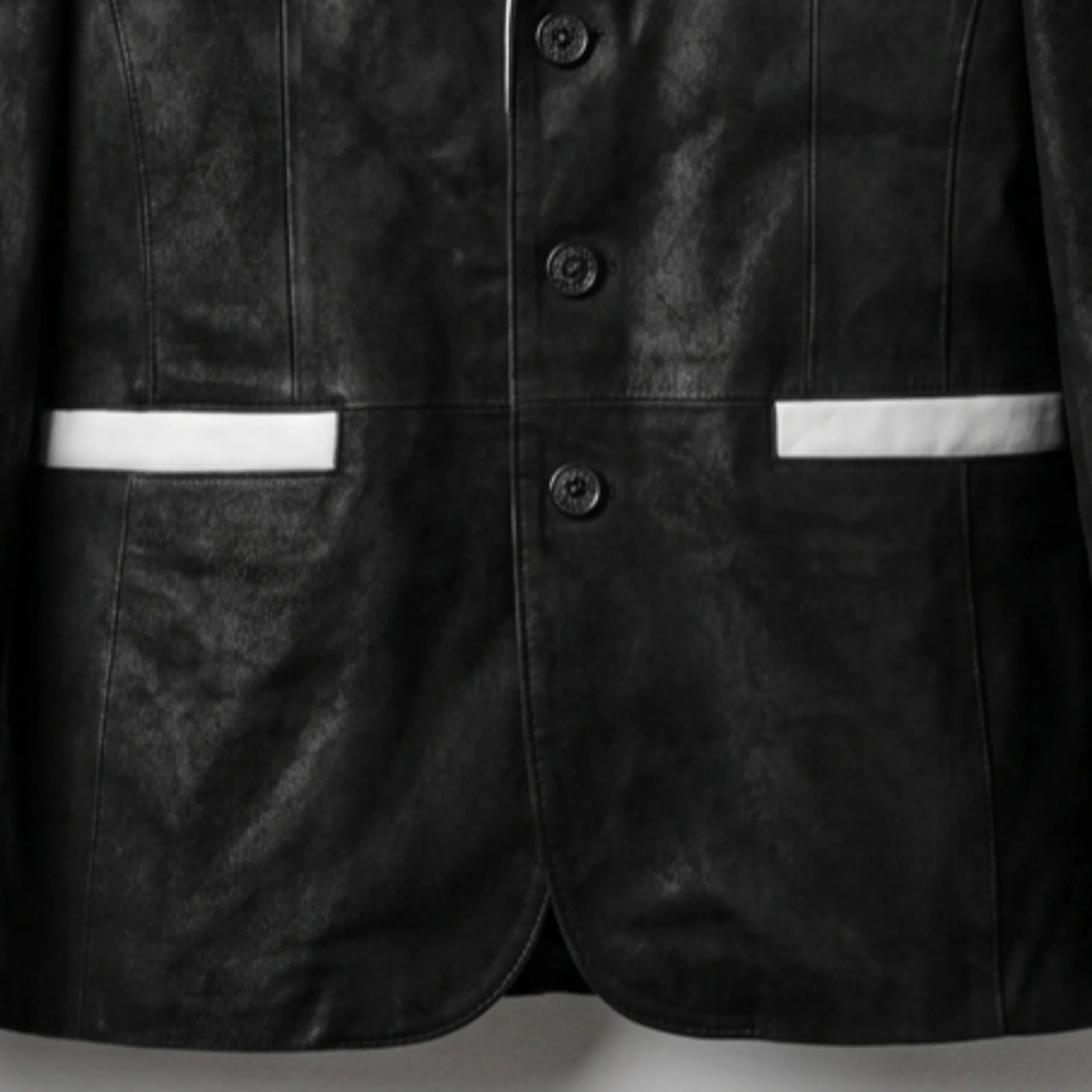 Front button and white pocket trim detail on men’s black and white leather blazer
