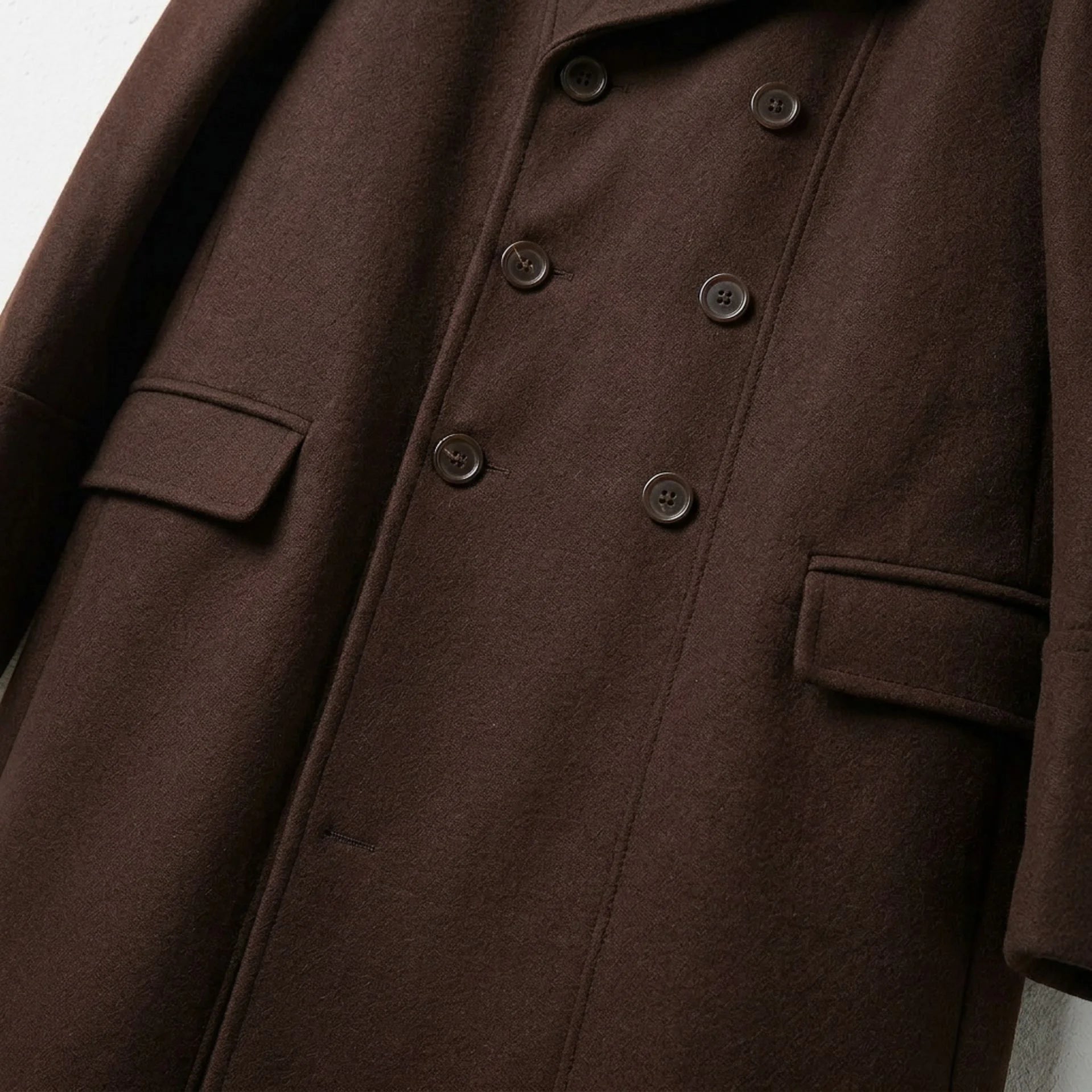Close up of buttons and flap pockets on men's brown double breasted coat.