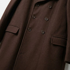 Close up of buttons and flap pockets on men's brown double breasted coat.