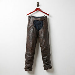 Front view of men's distressed brown leather motorcycle chaps with belt worn over black pants