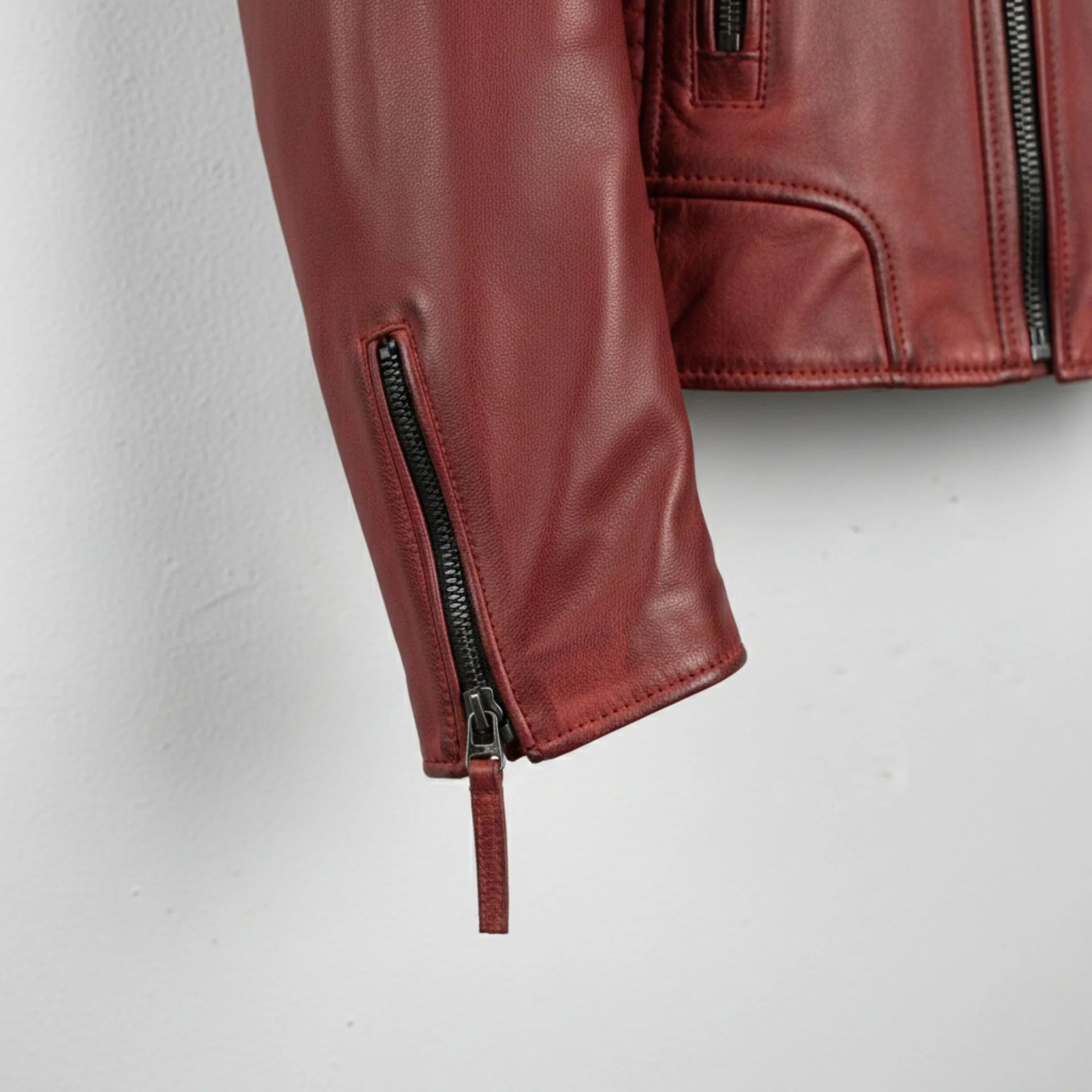 sleeve and cuff zipper close up on men's red leather motorcycle jacket.