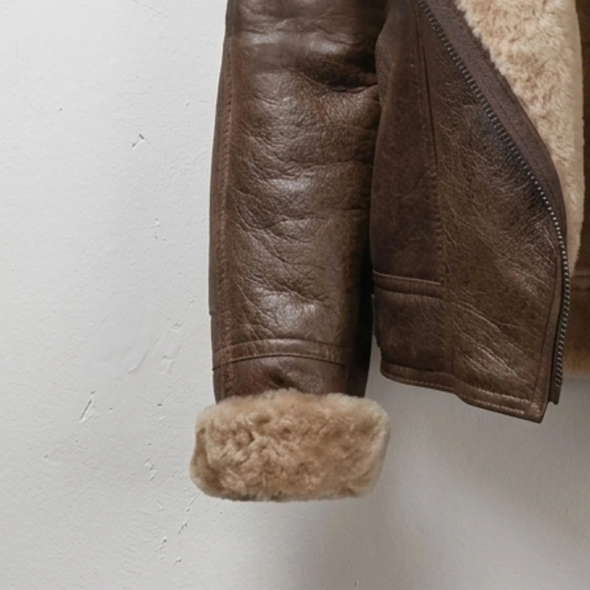 Close-up of brown leather sleeve with rolled shearling cuff on women’s jacket