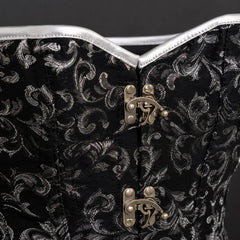 Close-up of black patterned corset front showing silver edging, detailed stitching and antique-brass-tone clasps