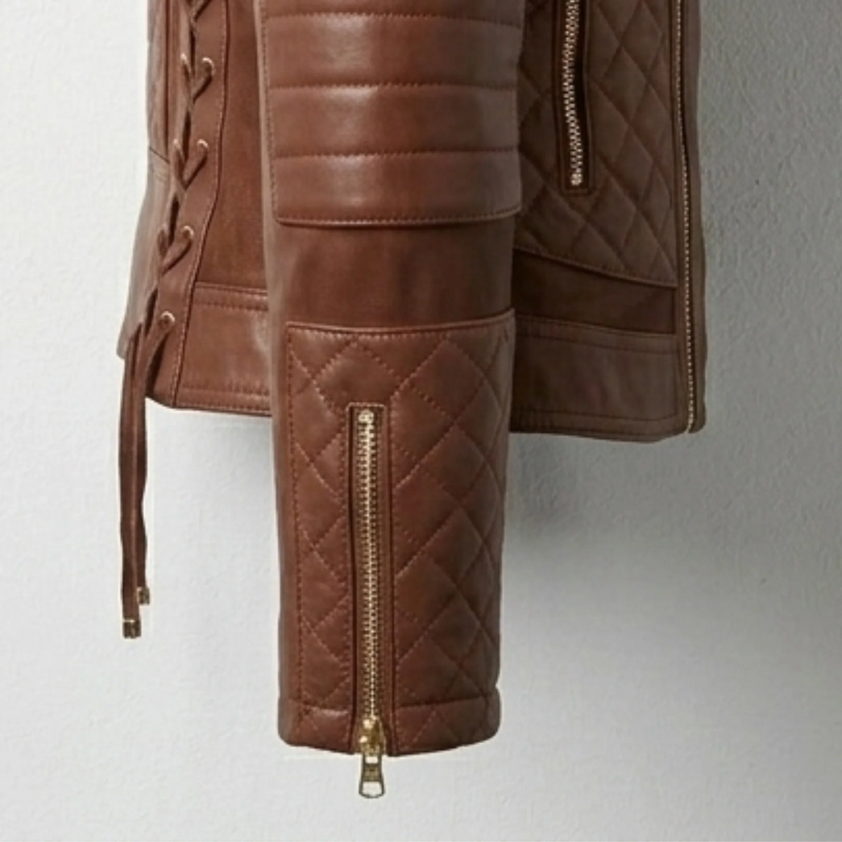 Detail of quilted sleeve, padded elbow and cuff zipper on women’s brown hooded moto leather biker jacket.