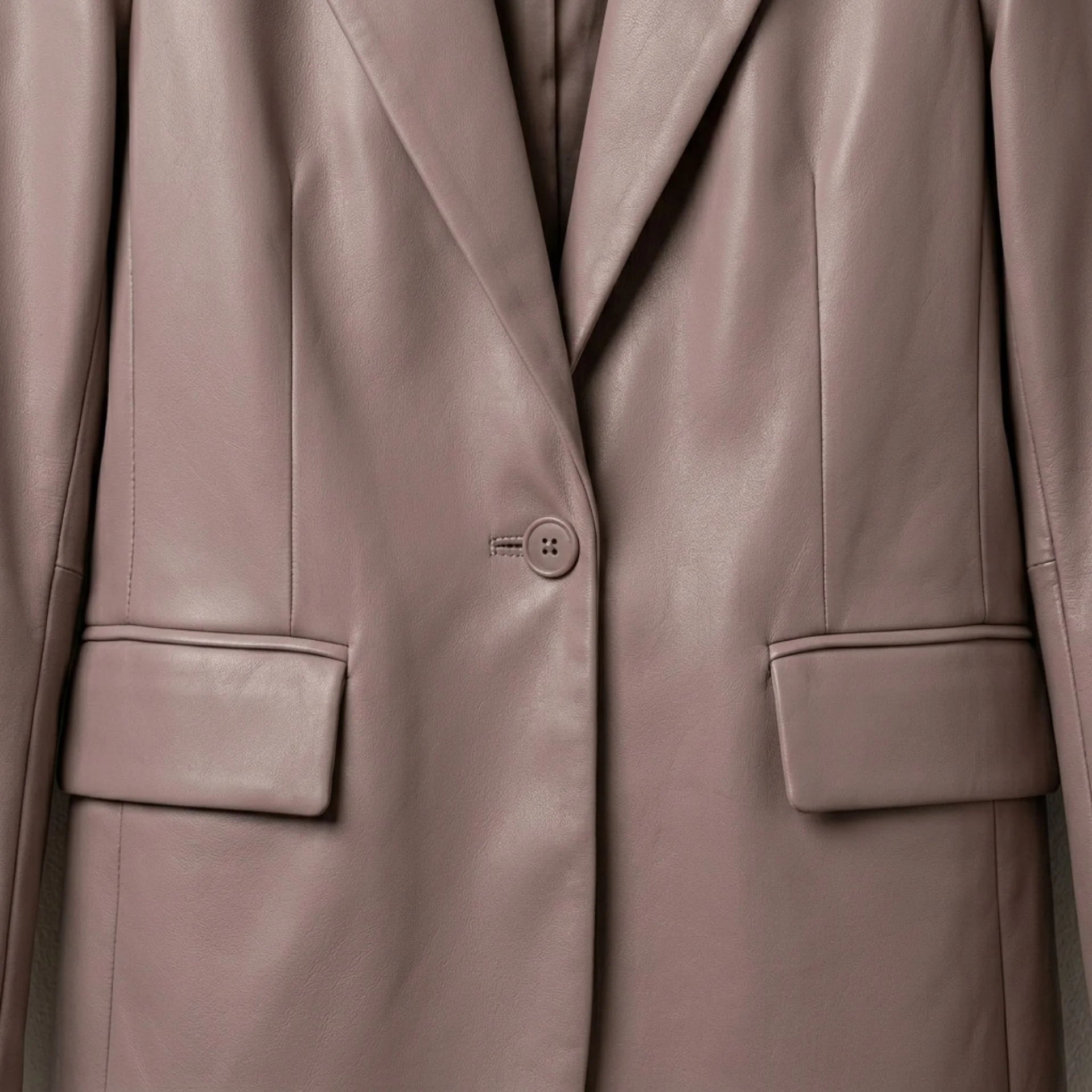 Close up of front button and flap pockets on women’s taupe leather blazer