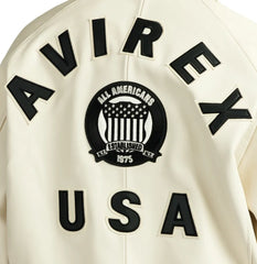 Close-up rear detail of Avirex beige Icon jacket showing black AVIREX lettering, heritage crest and USA appliqué