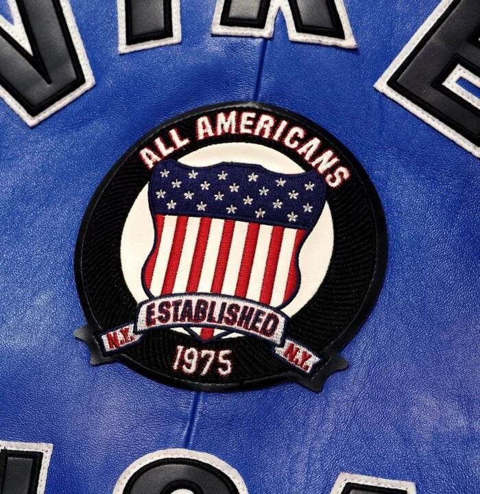 Close-up rear detail of Avirex blue bomber showing All Americans Established 1975 crest and surrounding lettering