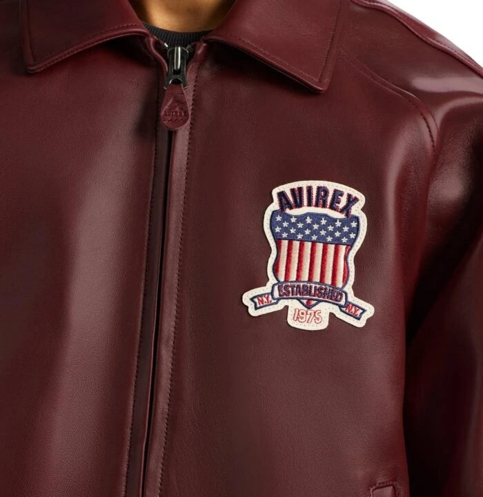 Close-up of maroon Avirex leather bomber showing USA heritage shield chest patch, collar and front zipper