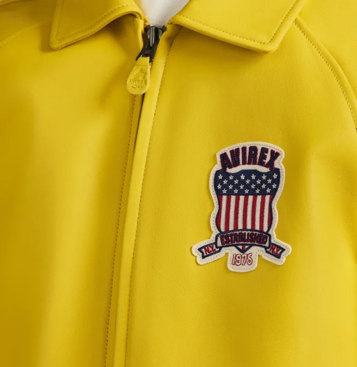 Close-up of yellow Avirex leather jacket showing heritage USA shield chest patch, fold-down collar and zipper