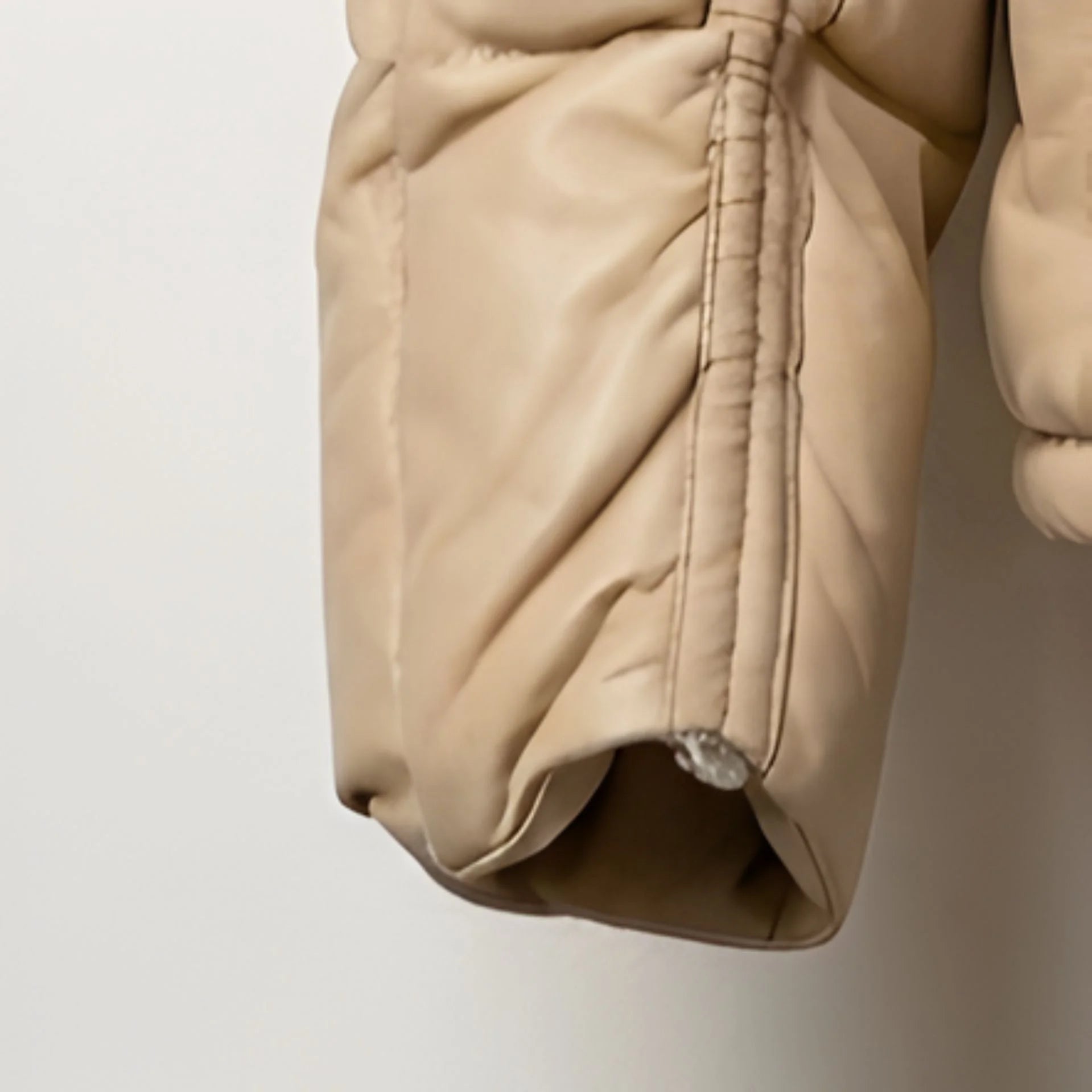 Close‑up of sleeve cuff and quilting on beige leather puffer coat.