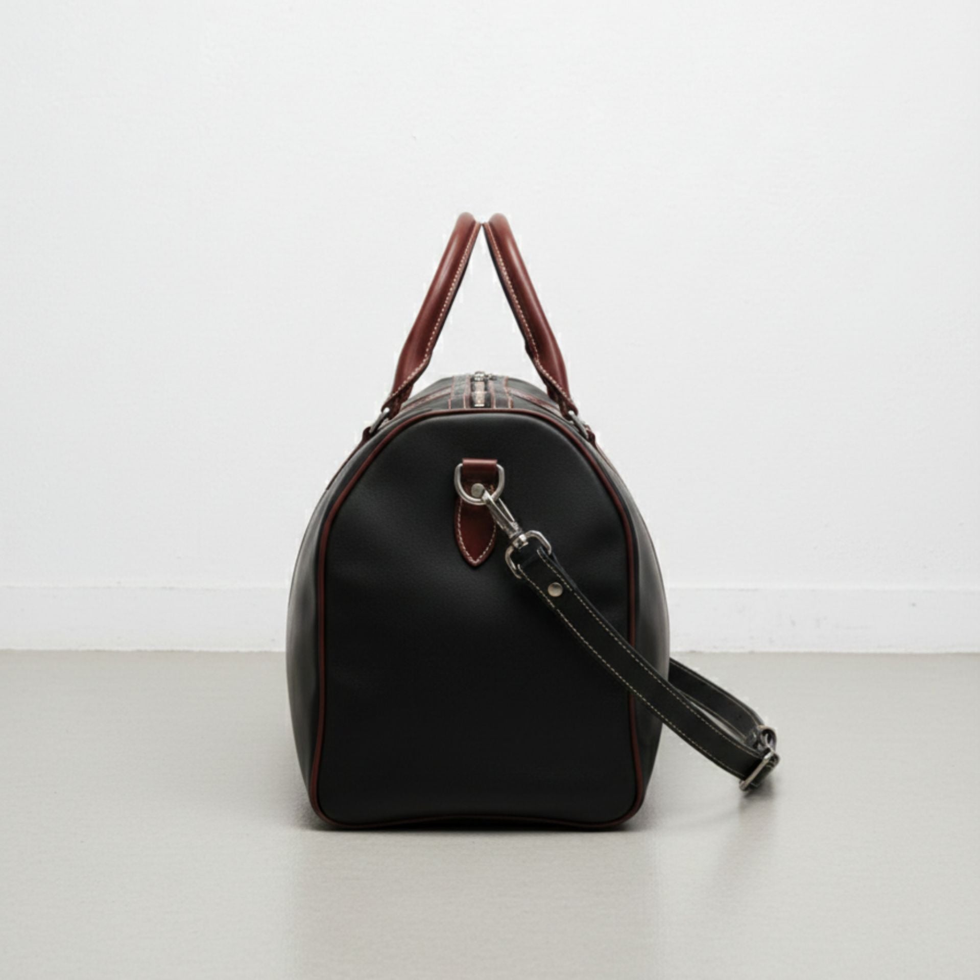 side view black and brown leather weekender bag with detachable strap.