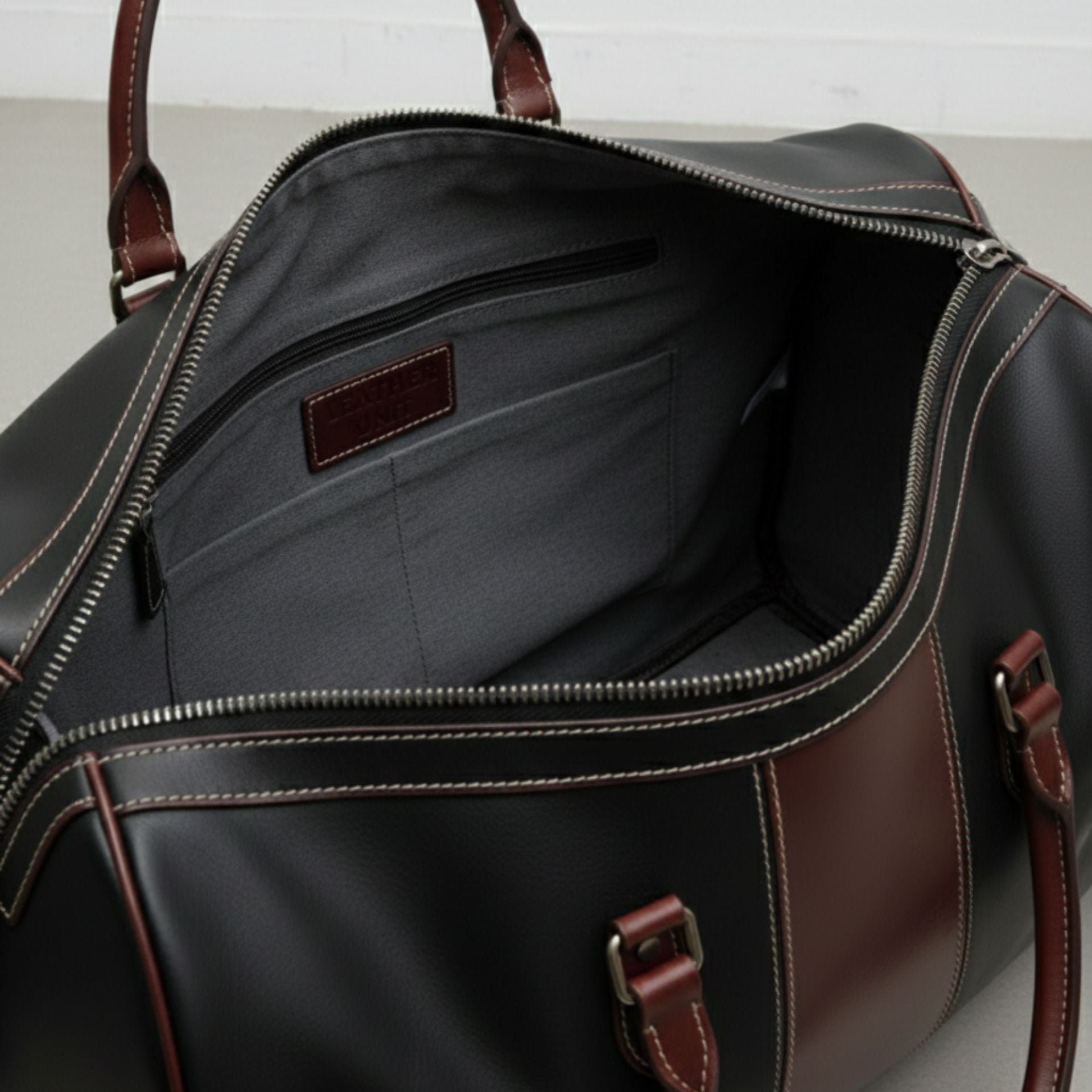 interior of black and brown leather duffle bag with grey lining and zip pocket.