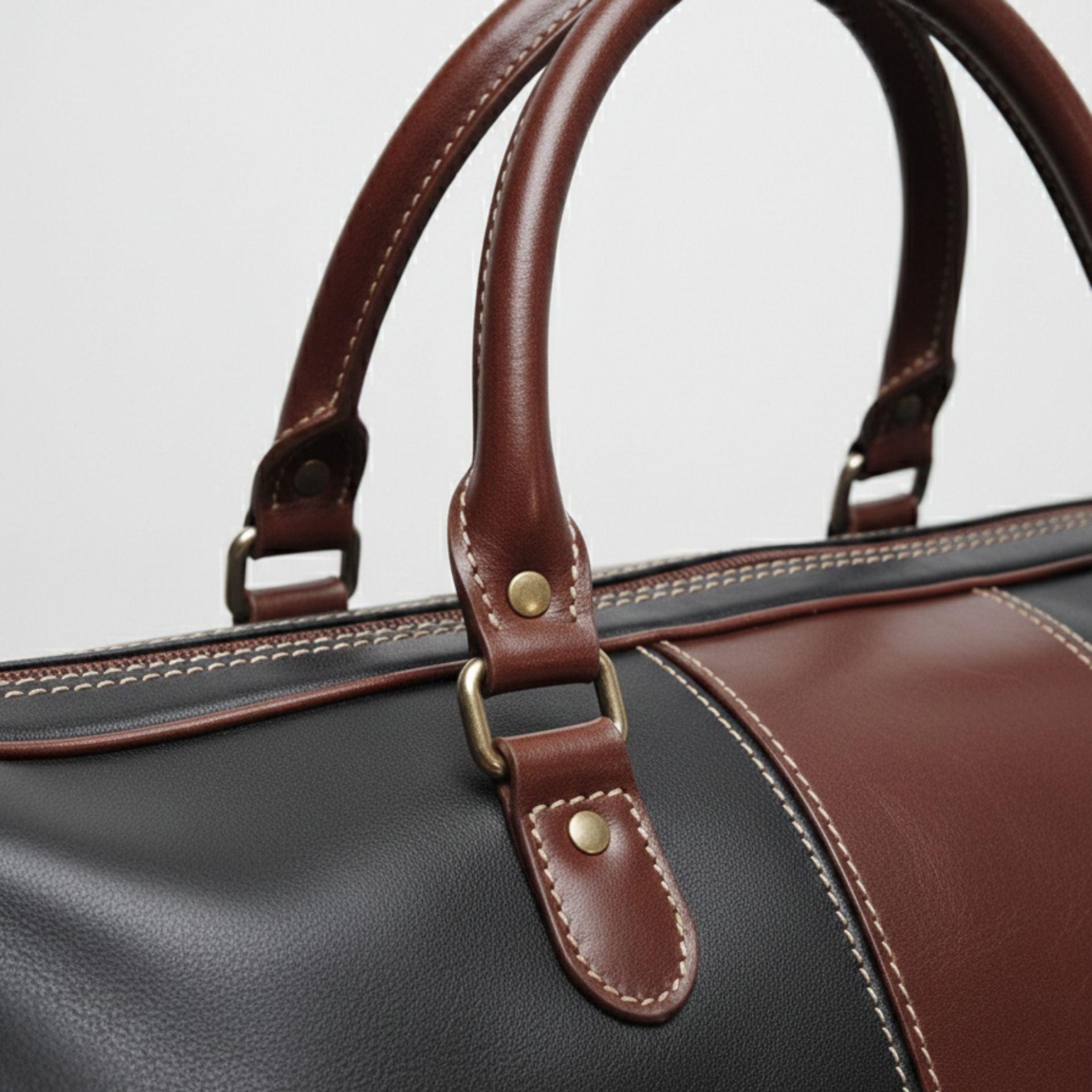 close up brown leather handles and hardware on black travel duffle bag.
