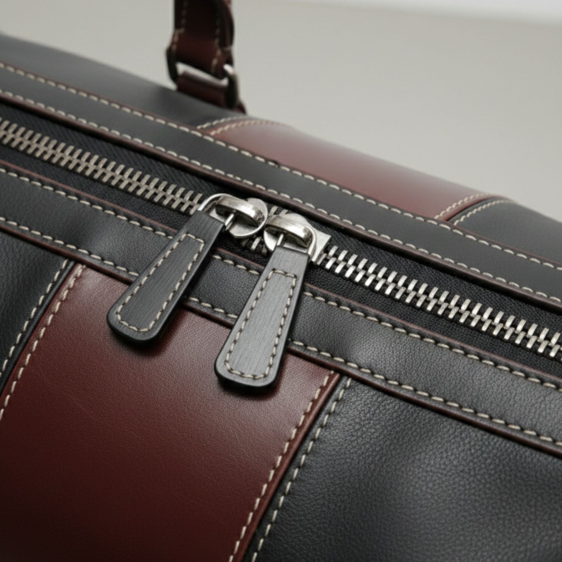 close up silver double zipper and stitching on black and brown leather duffle.