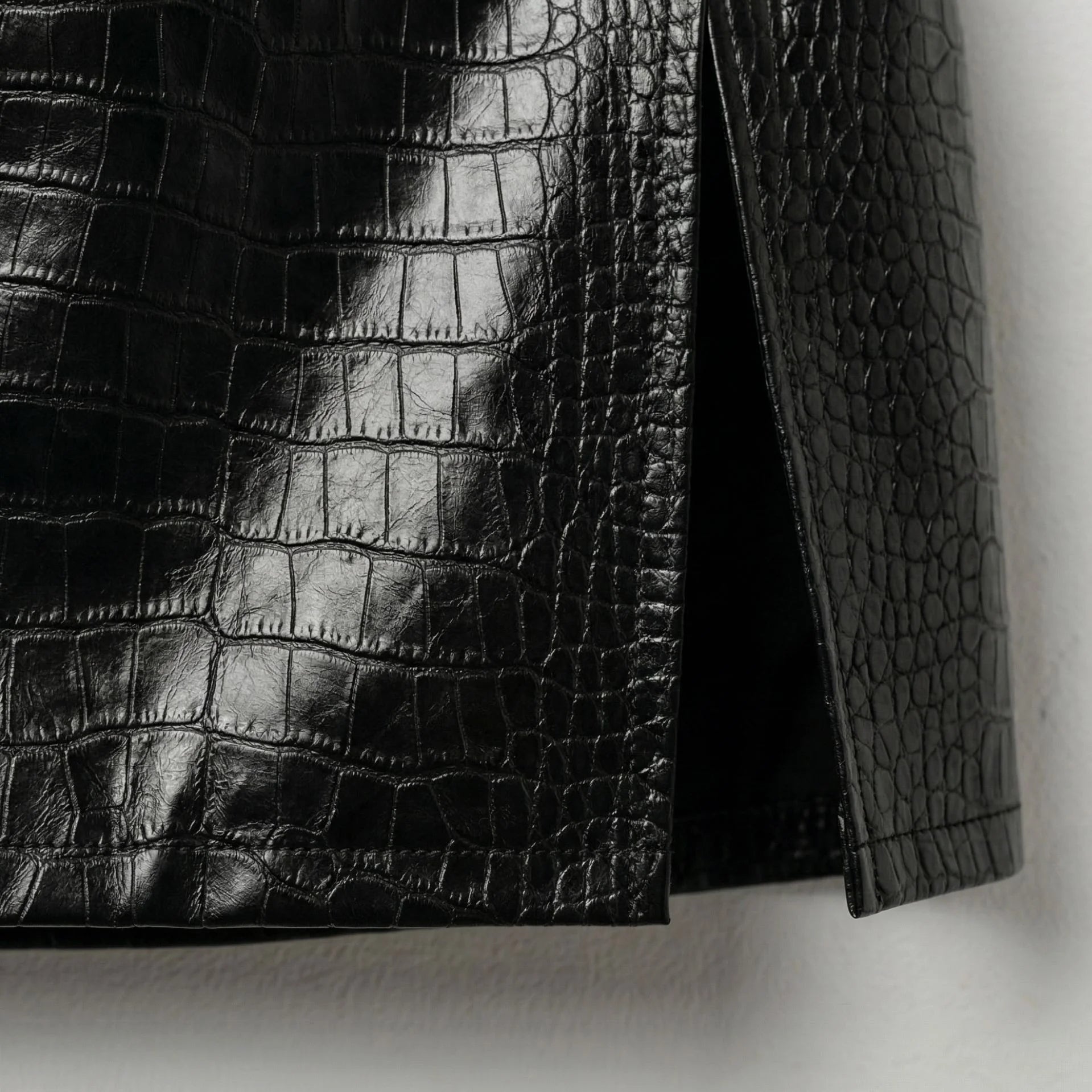 Close up of side slit and hem on black crocodile leather mini skirt