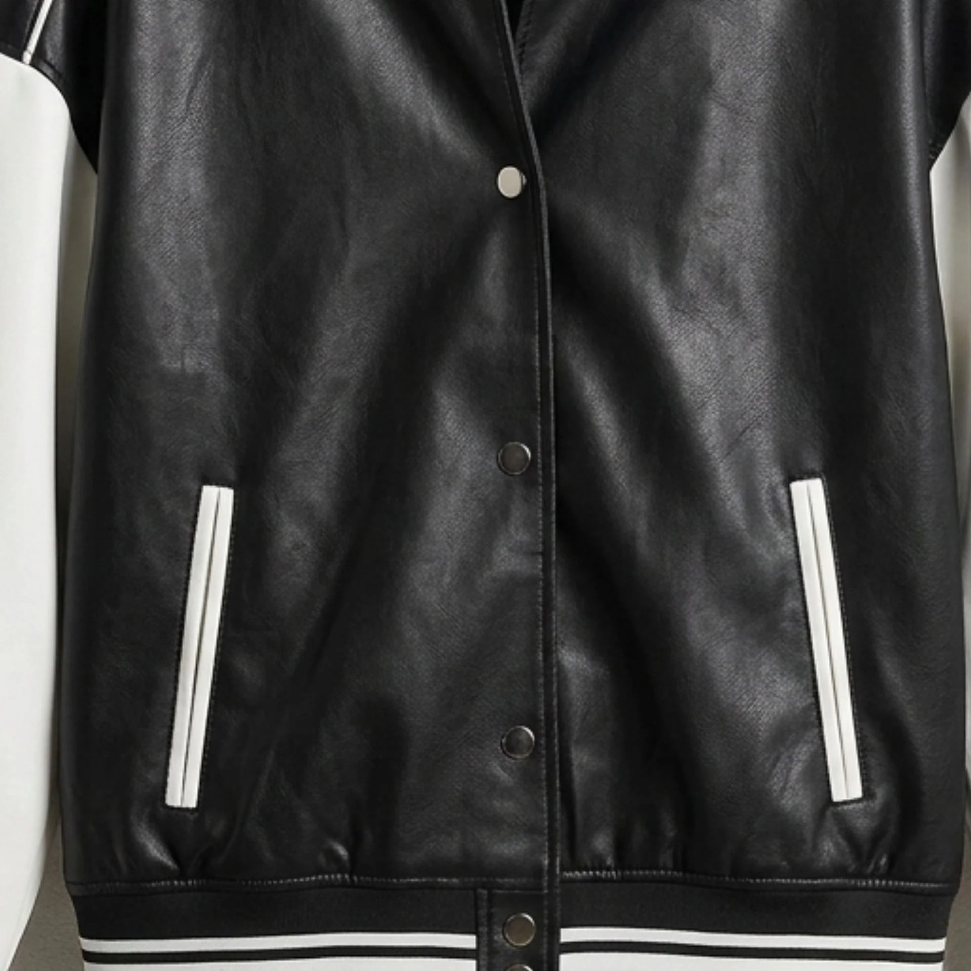 Front snap buttons and welt pockets on black and white leather varsity jacket