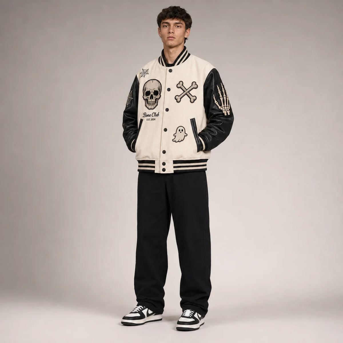 Three-quarter view of bone-white Halloween varsity jacket with black faux leather sleeves and skull patch details