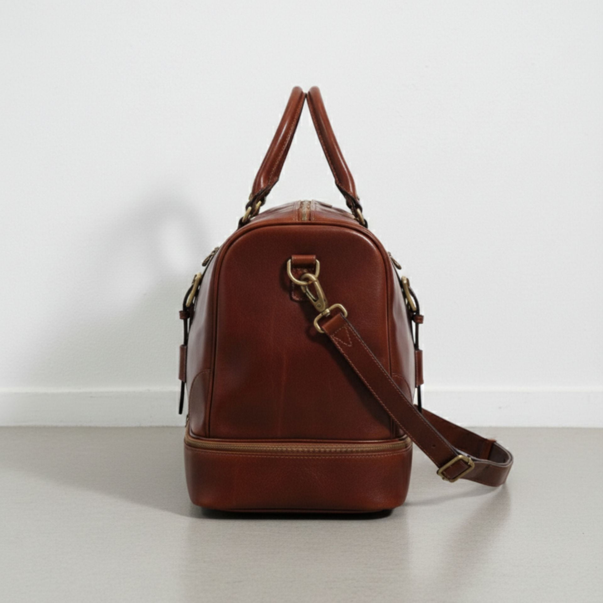 side view brown leather weekender bag showing drop bottom zipper compartment.