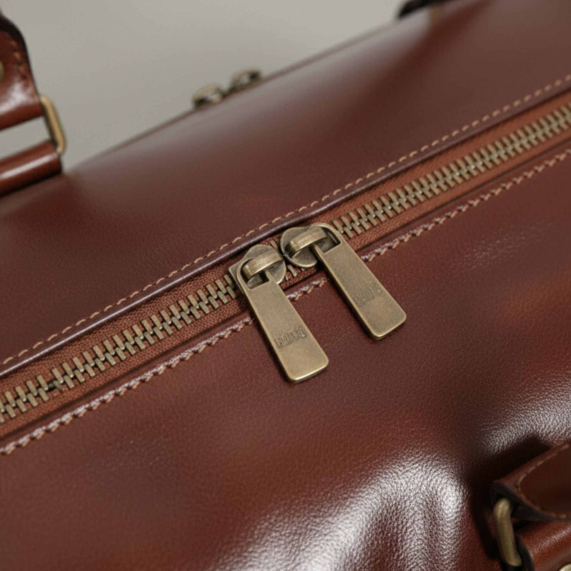 close up of brass metal zippers on brown genuine leather drop bottom bag.