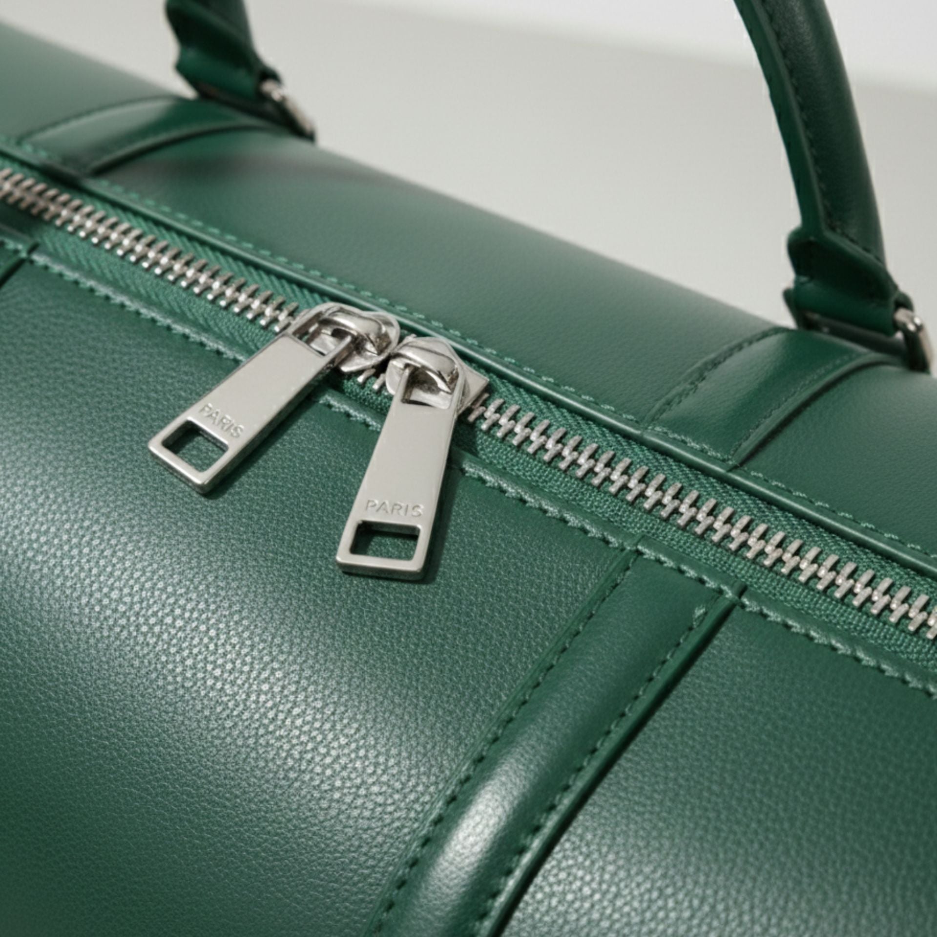 close up of silver double zipper on green genuine leather travel bag.