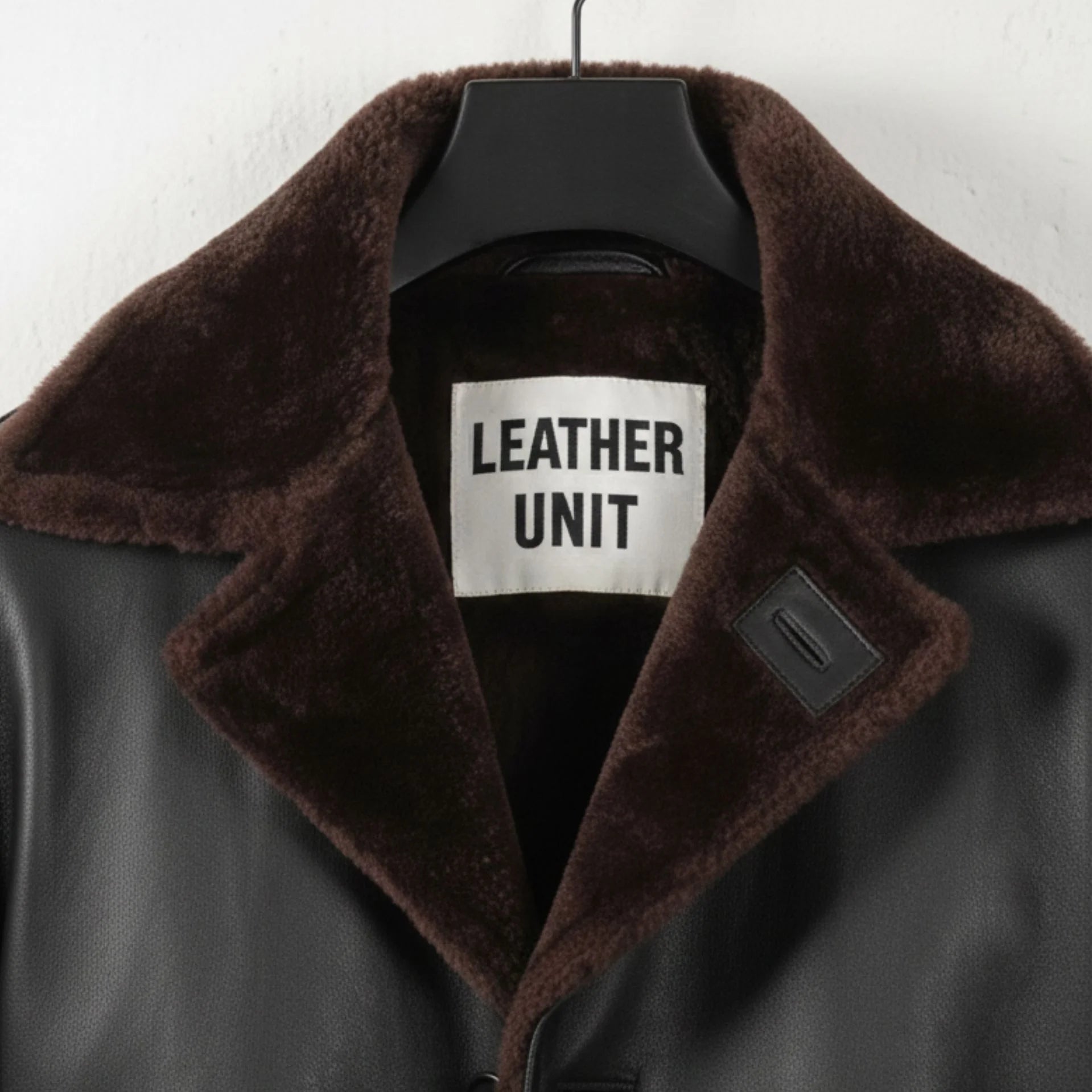 Close up of brown shearling collar and Leather Unit label on black coat