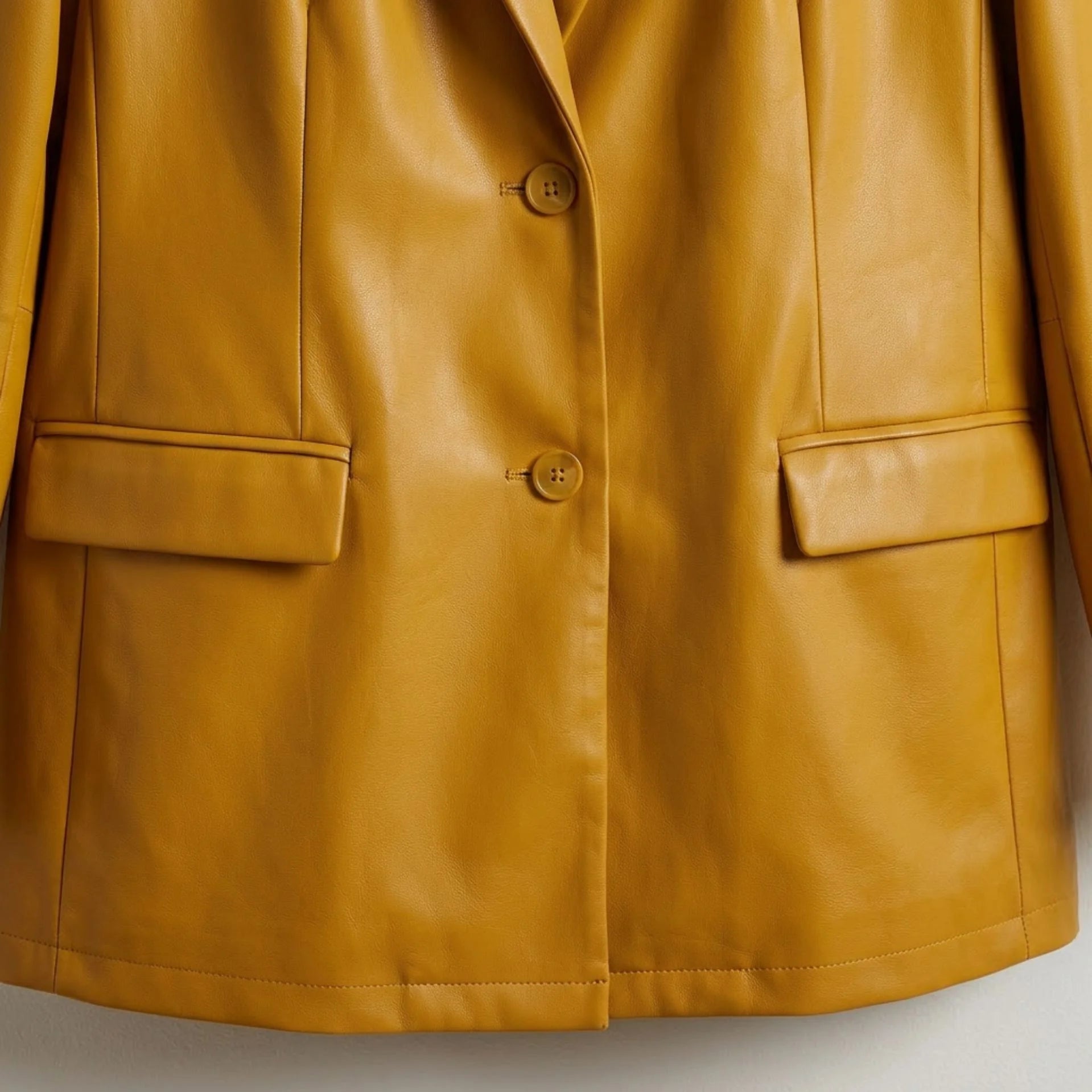 Two‑button front and flap pockets on women’s mustard yellow leather blazer
