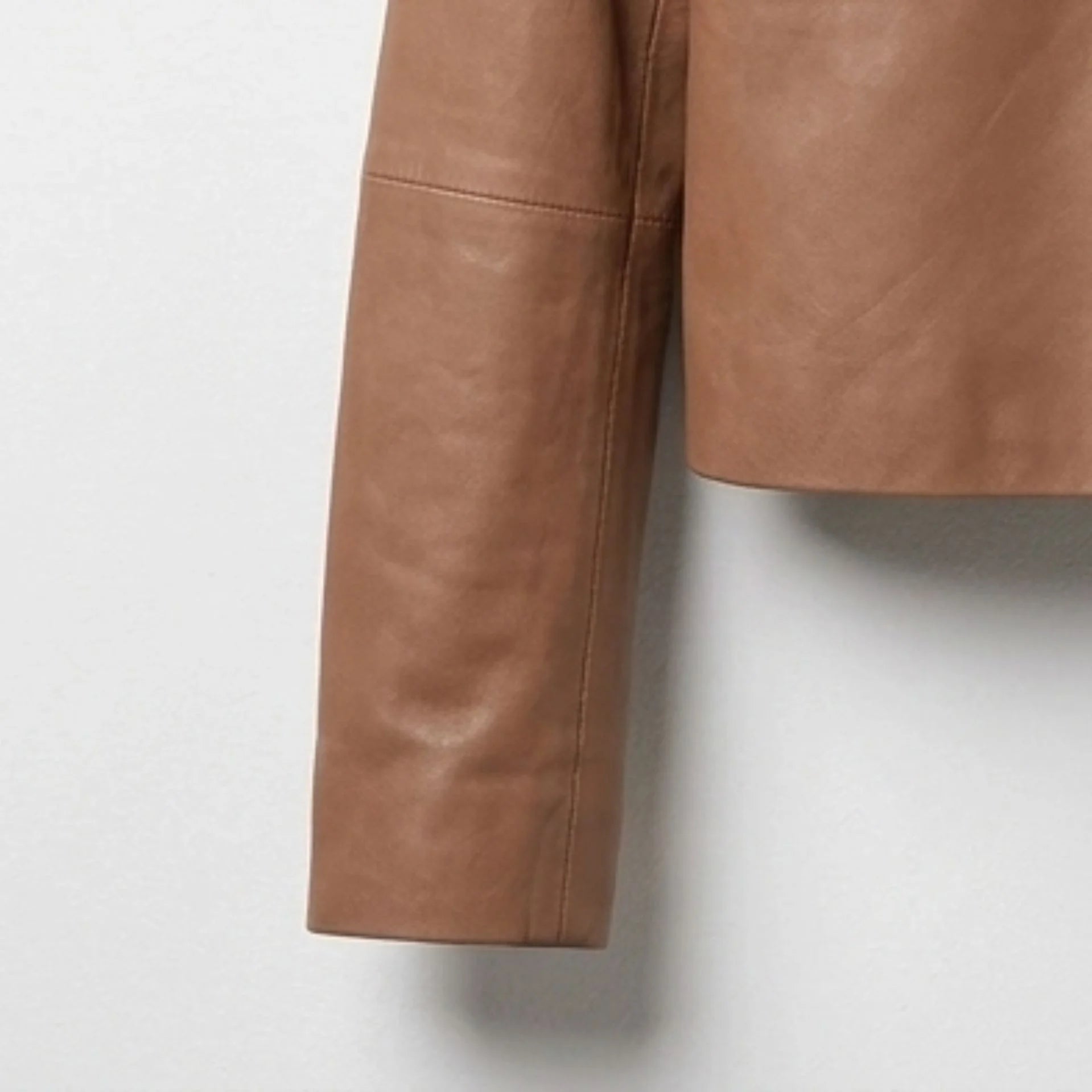 Close-up of sleeve and hem detail on a women's tan cropped leather shirt jacket