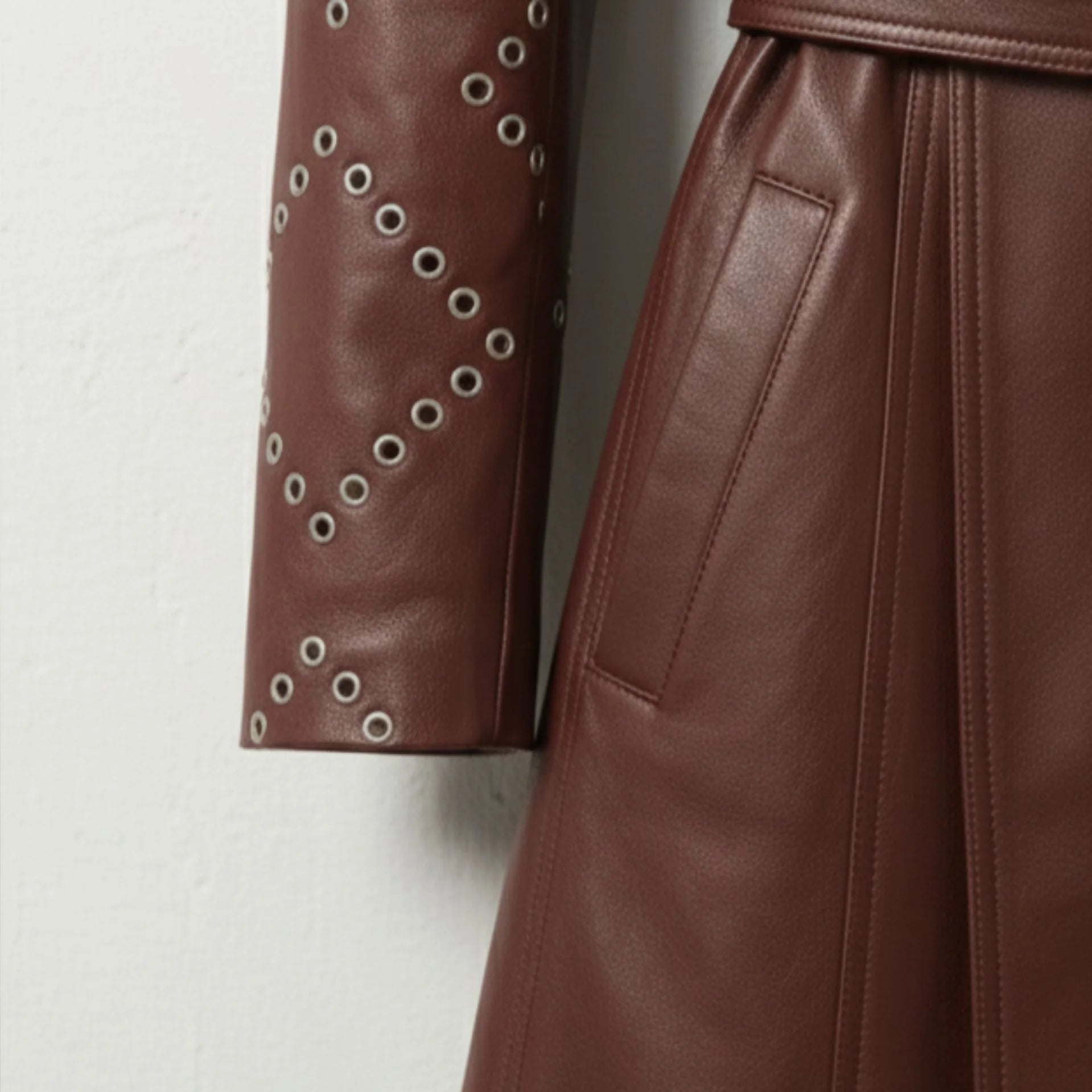 Sleeve stud and pocket detail on women’s maroon leather trench coat