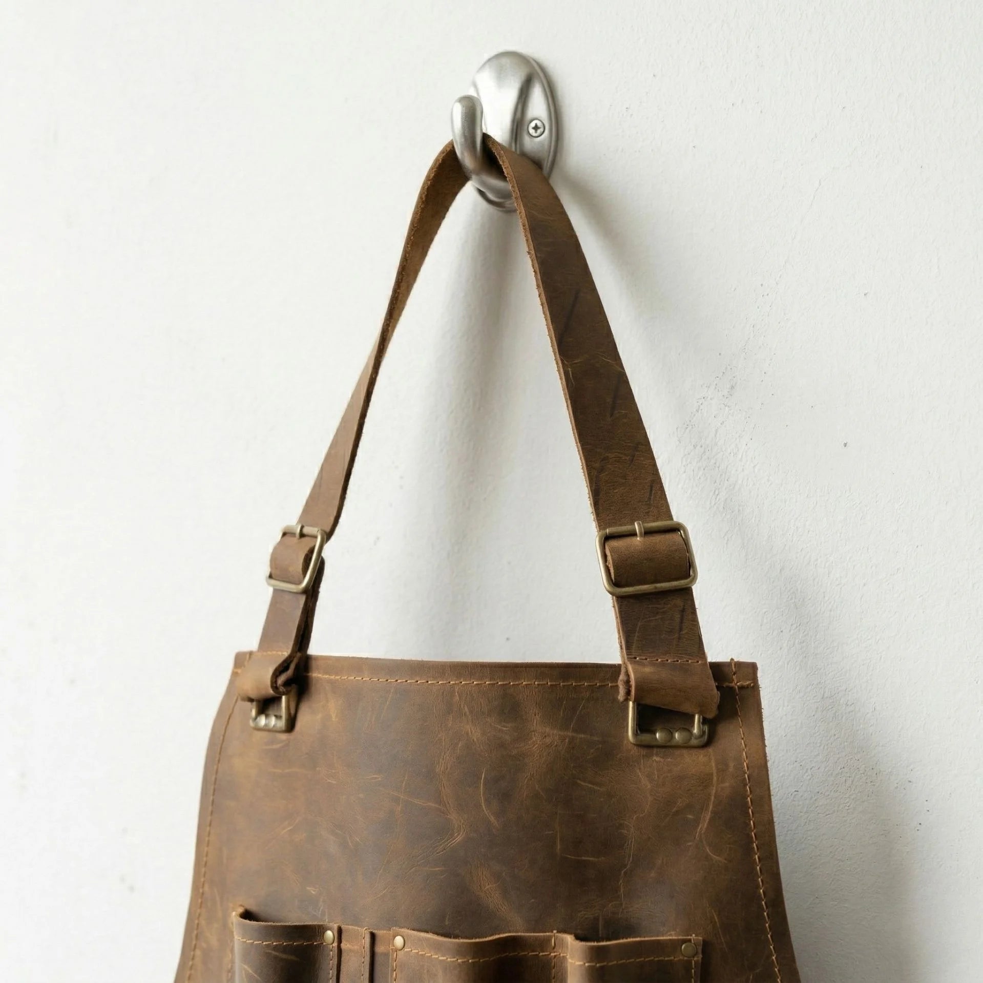 Top strap detail of brown leather workshop apron hanging on hook