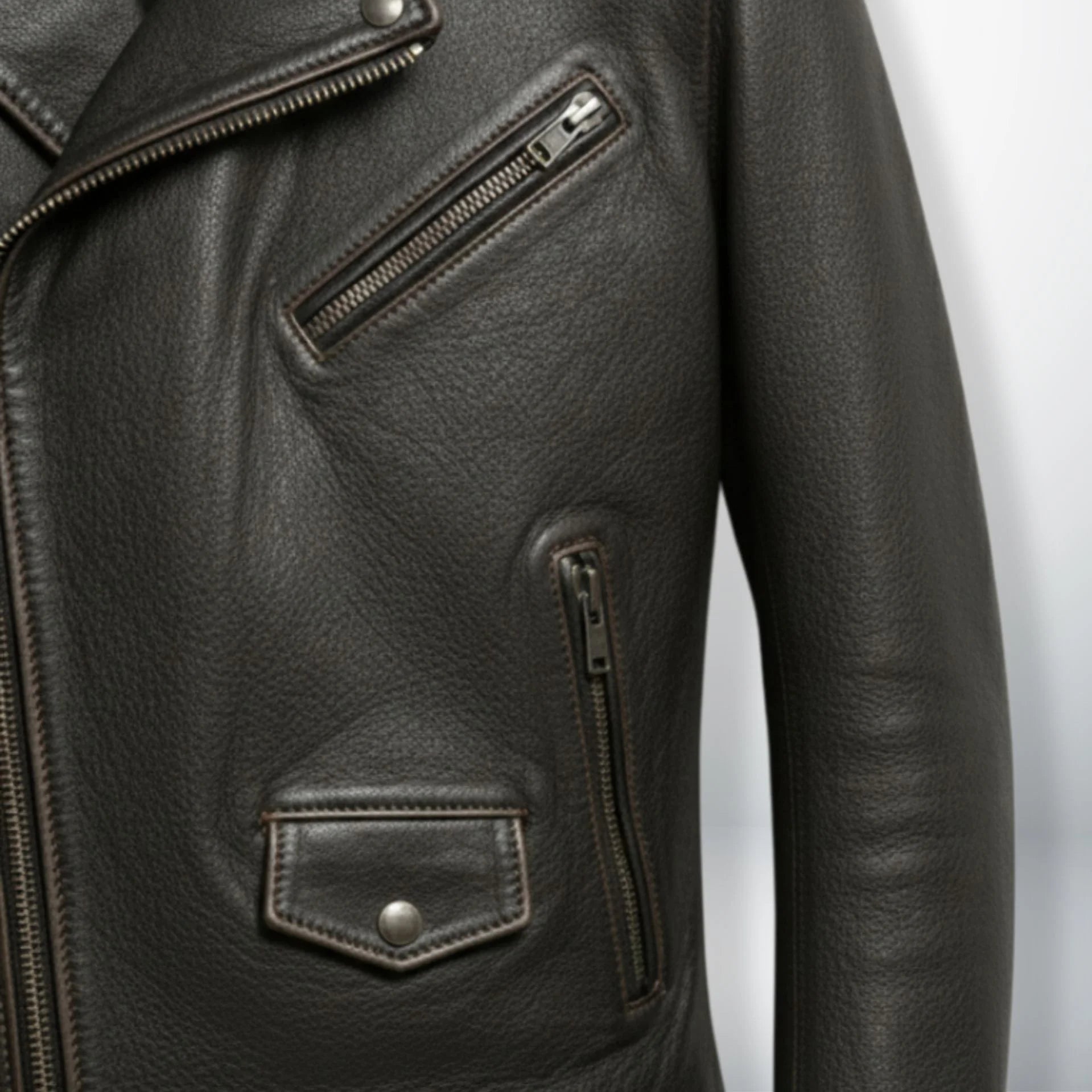 detail of chest zip pocket and flap pocket on men's dark brown leather jacket.