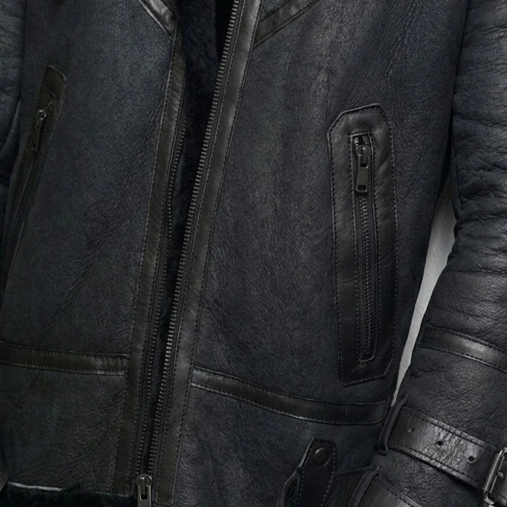 close up zipper pockets and grain on mens black shearling bomber leather jacket.