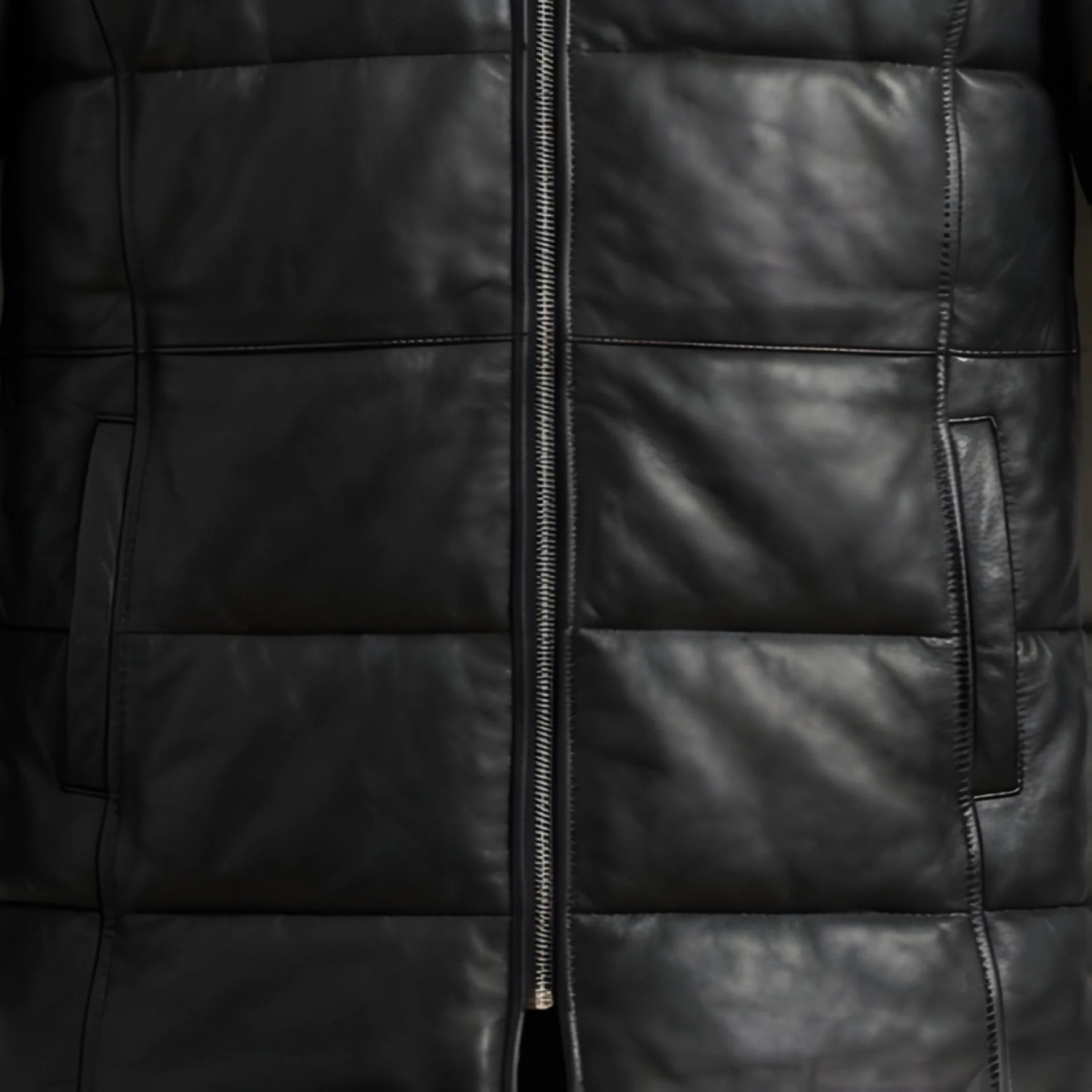 Close up of front zipper and hand pockets on men's black hooded leather winter coat.