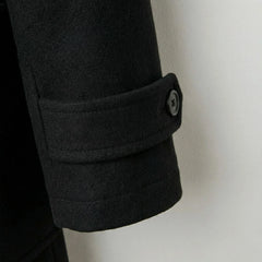 Detail of cuff strap and button on men's black wool duffle coat.